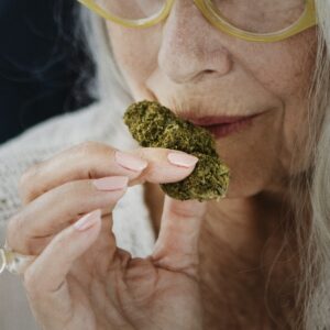 Older woman gently smelling a cannabis bud to evaluate terpenes and aroma, showcasing sensory engagement with the plant.